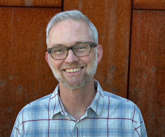 Jeffrey S. Chapman smiling in front of a rust-colored metal wall